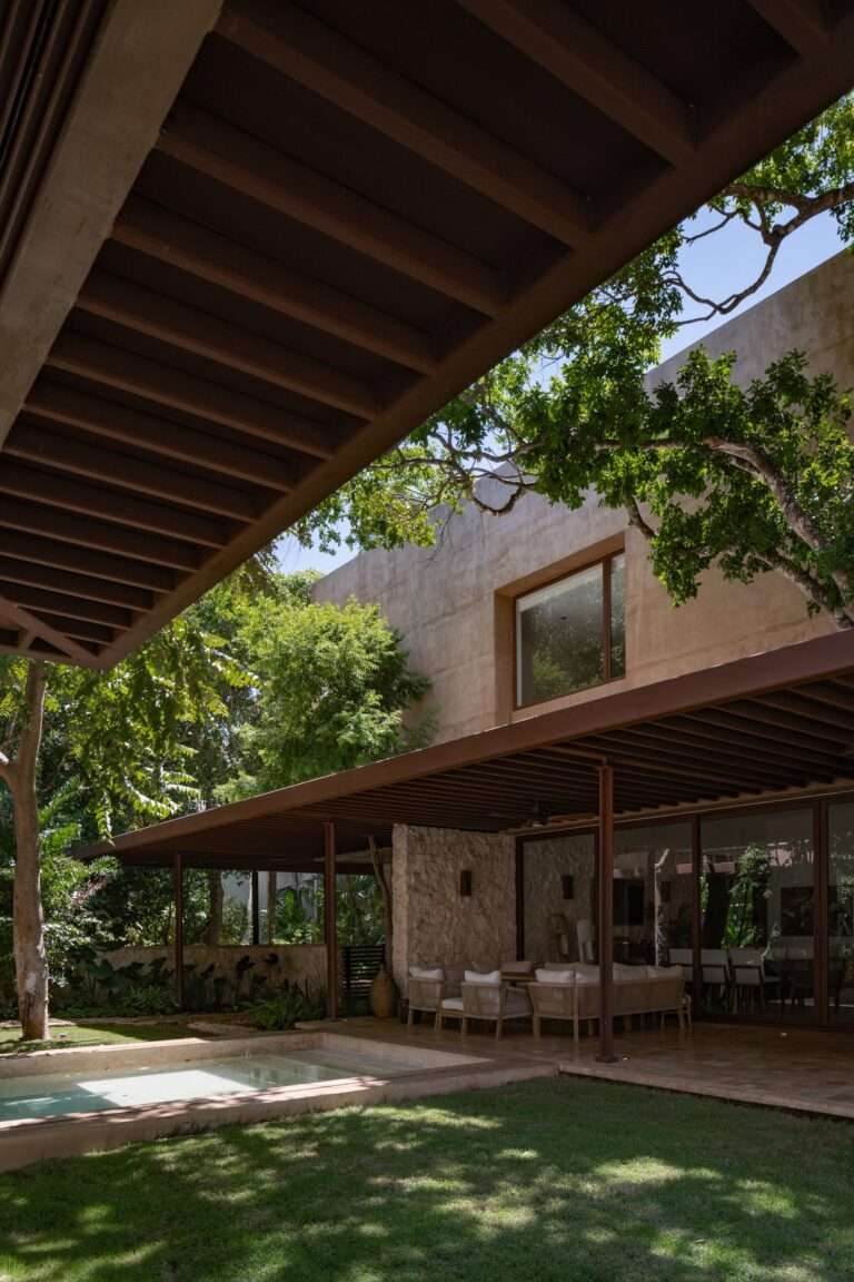 View looking up at the upper volume of Casa Sudzal from the pool deck, showing lime-plastered walls and steel canopy framing.