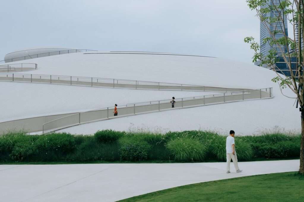 People walking along a white sloped ramp integrated into the curved roof of a cultural pavilion at Shenzhen Bay Culture Square.