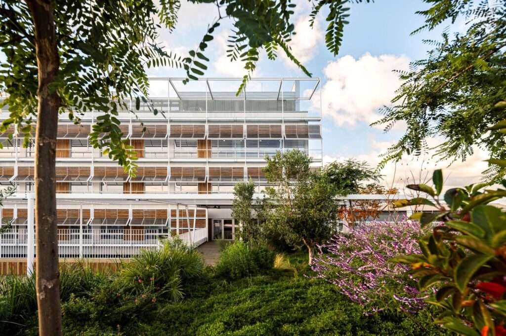 Lush green garden terrace in front of the modular louvered facade of Hospital del Mar expansion.