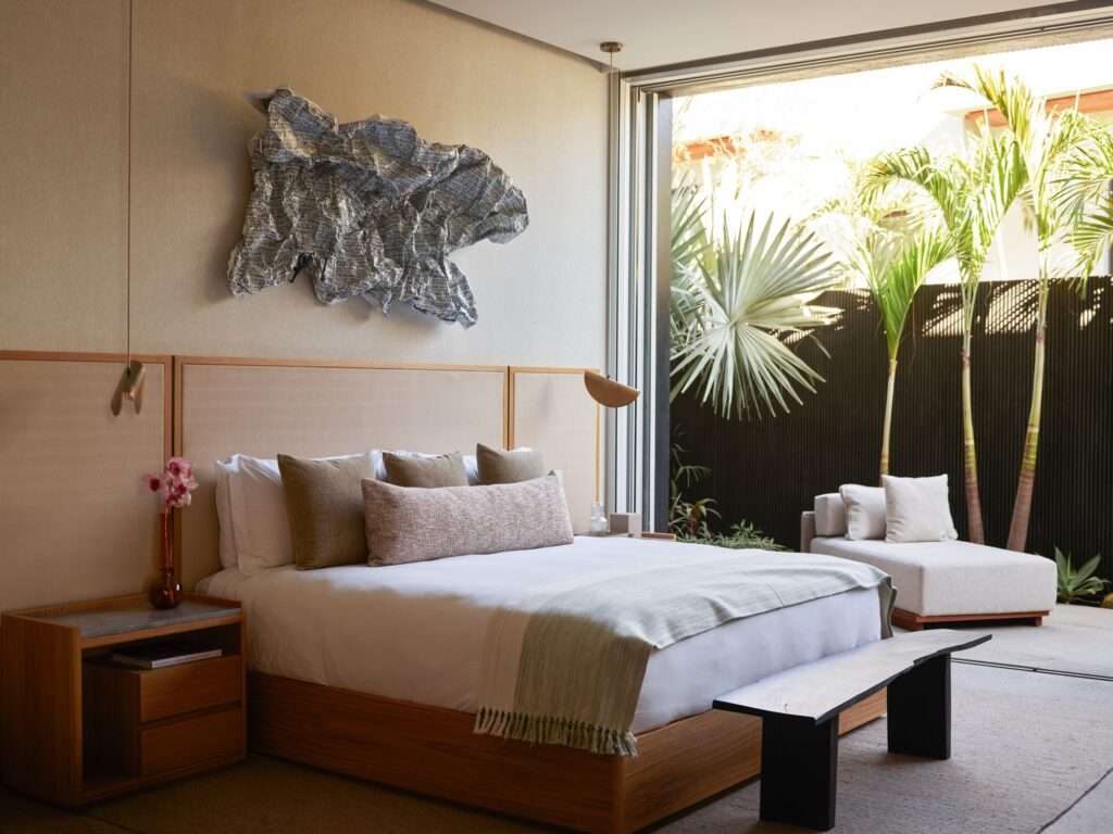 Modern bedroom interior opening directly to a private patio surrounded by palm trees and dark wood-paneled walls.