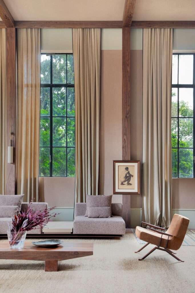 Low-profile modular sofa and wooden coffee table arranged in front of tall windows with framed artwork on a timber column.
