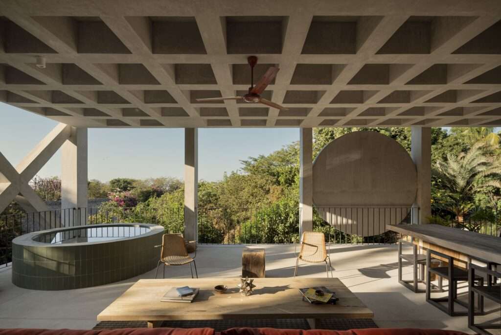 Covered outdoor lounge area with an oval green-tiled pool, lounge chairs, a low coffee table, and views toward the surrounding tree canopy.