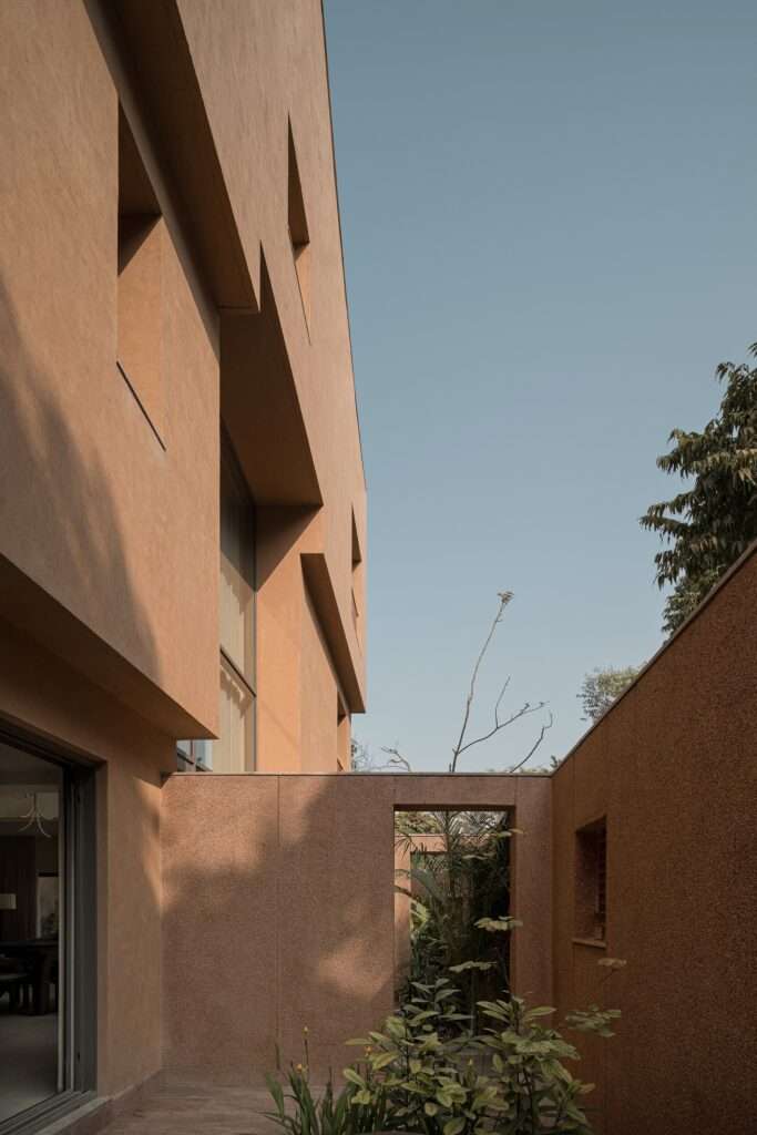 Narrow outdoor courtyards and peripheral boundary walls rendered in textured plaster with lush tropical planting adjacent to floor-to-ceiling glass doors.