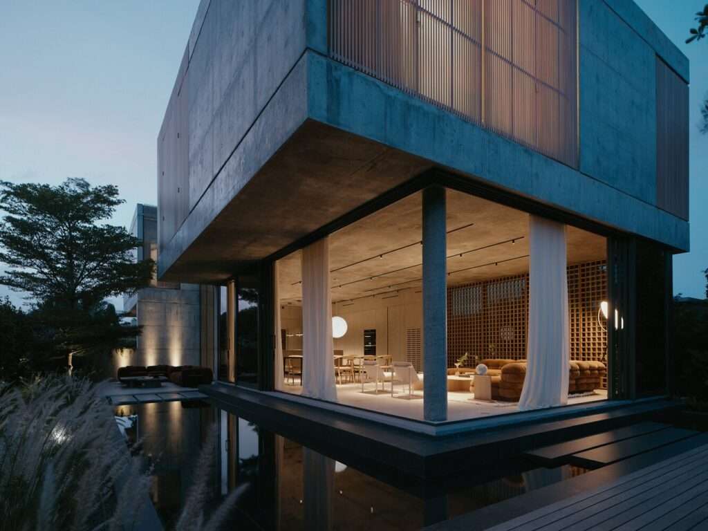 Exterior dusk view of Cherokee House showing illuminated interior living spaces framed by concrete overhangs and reflection pool.