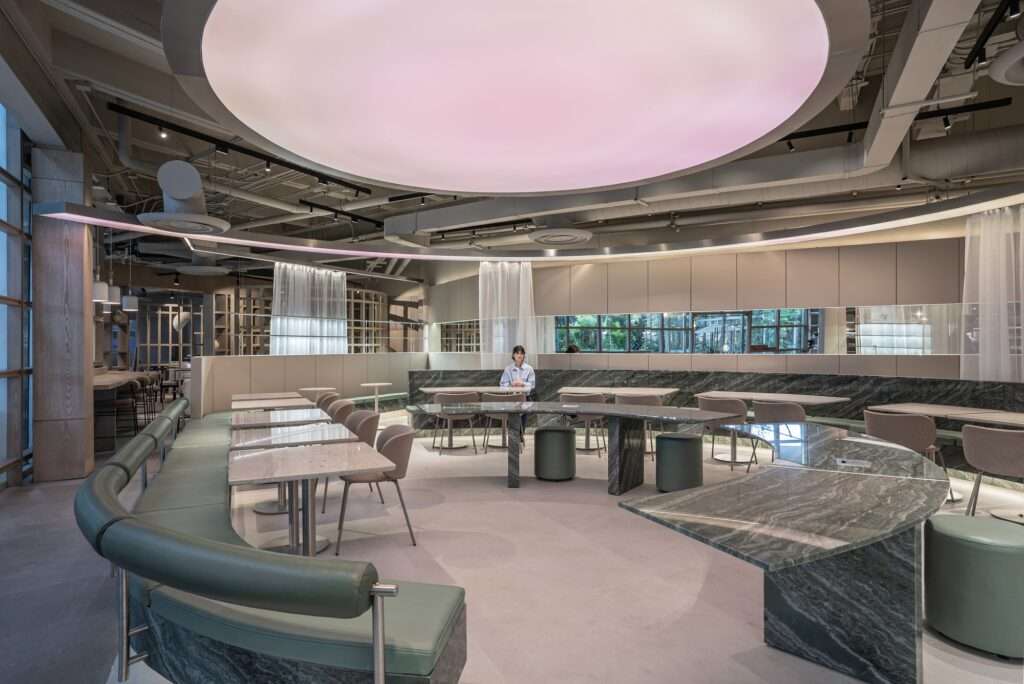 Wide view of Raheeq Ohm interior showing central circular seating, green quartzite counters, and ceiling lightbox.