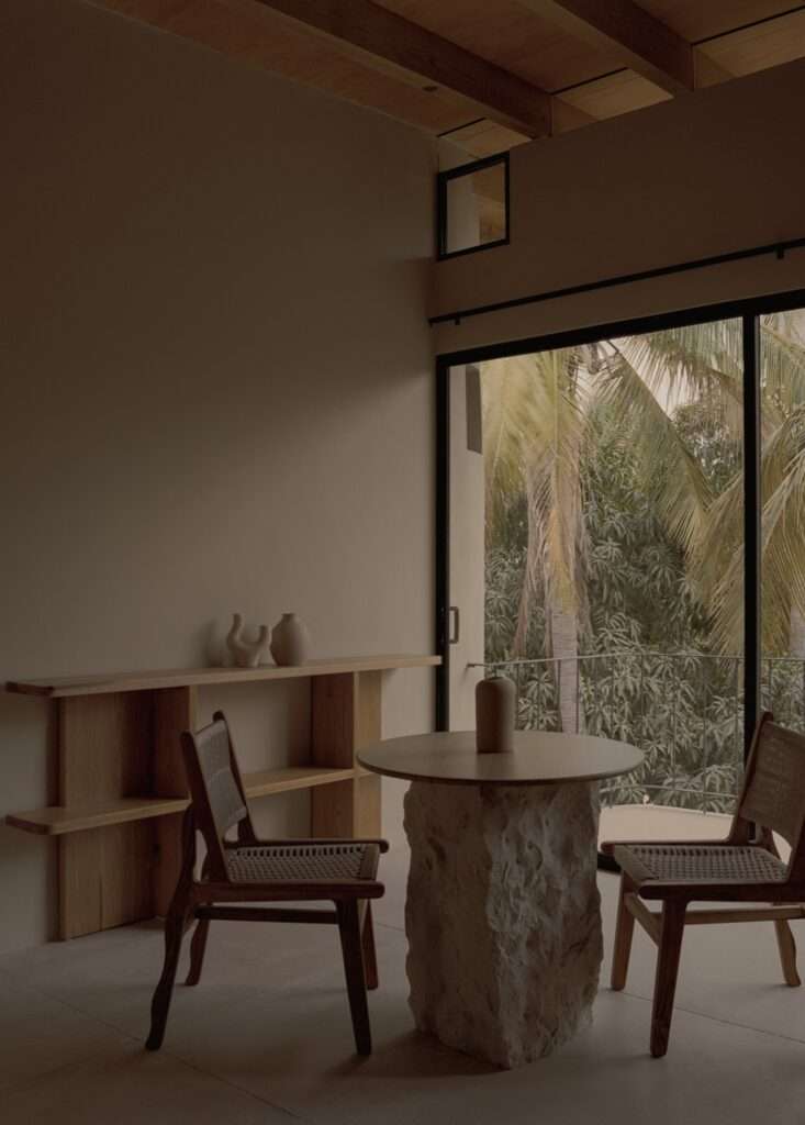 Dining nook featuring a carved stone pedestal dining table, woven wooden chairs, and views of palm trees through sliding glass doors.