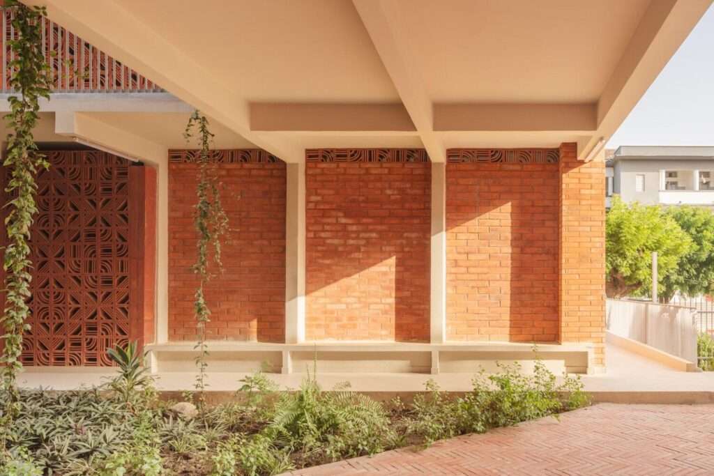 Ground-floor sheltered patio area with solid red brick walls, concrete structure, and climbing plants in a rain garden.