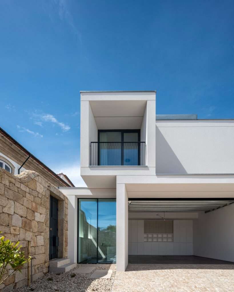 Entrance zone with glass paneling connecting a historic stone wall to a modern white garage and upper balcony structure.