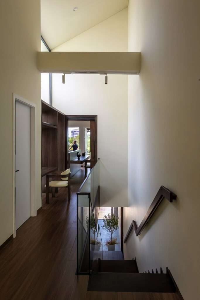 Interior corridor featuring dark wood flooring, a glass handrail staircase leading down, a recessed study desk area, and double-height ceiling space filled with natural light.
