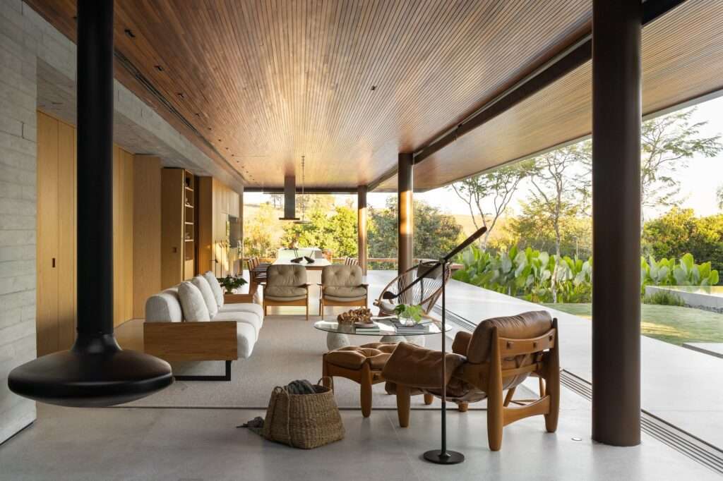 Wide interior view looking down the open-plan living and dining area of Casa da Mata with leather lounge seating, cylindrical columns, and landscape views.