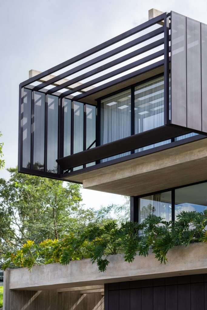 Low-angle exterior shot showing the cantilevered steel frame and perforated metal screen extending beyond the concrete base of Casa Galería.