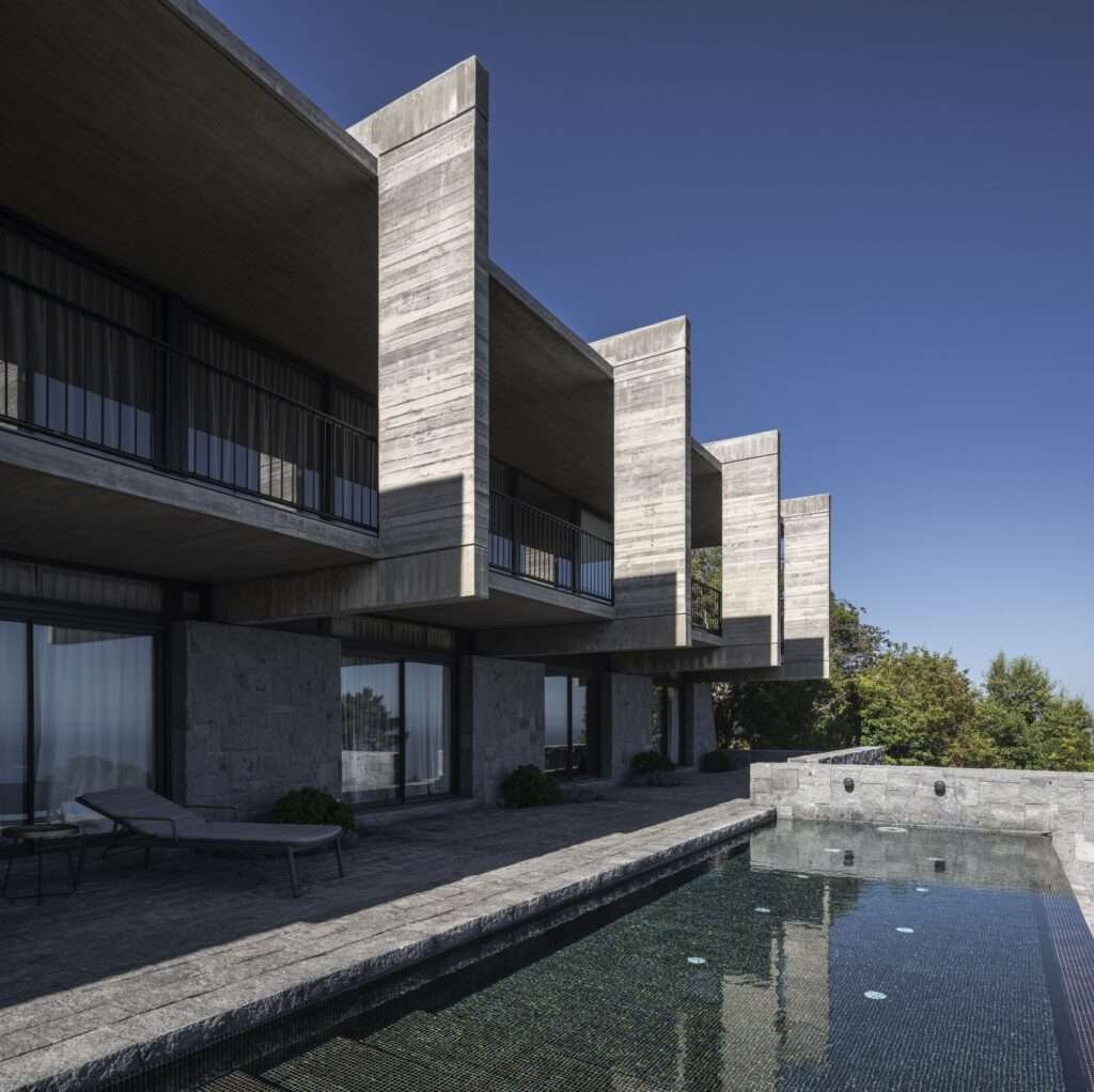 Lap pool adjacent to a heavy stone retaining wall underneath the cantilevered upper concrete volume of Casa Zapallar.