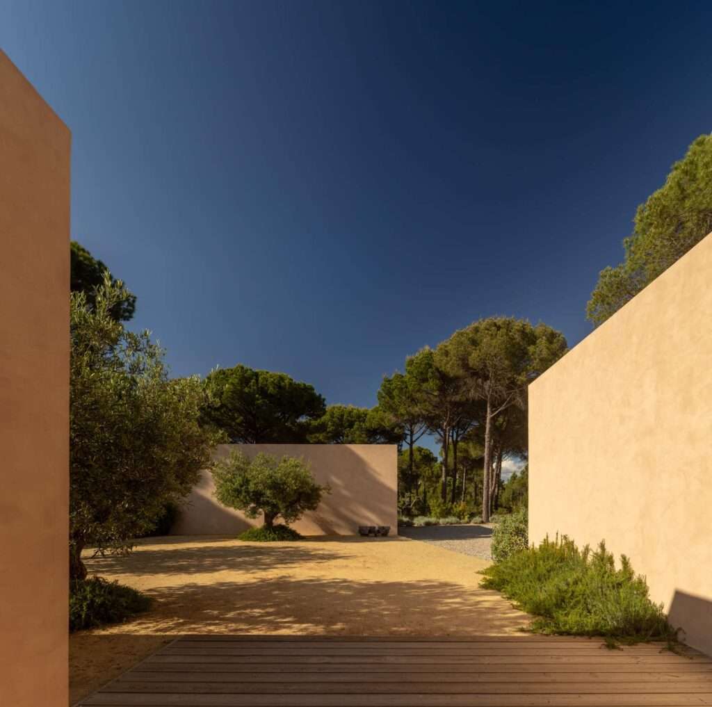 Open-air gravel courtyard enclosed by minimalist earth-toned walls and olive trees at Muda L13.