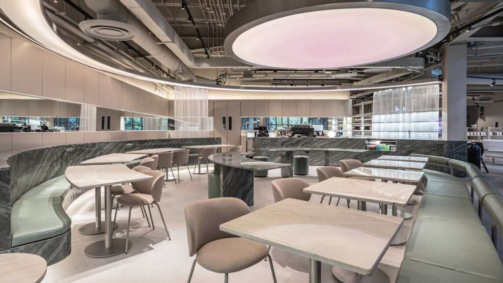 Interior dining area of Raheeq Ohm featuring beige quartzite tables, green banquette, and mirror strip wall.