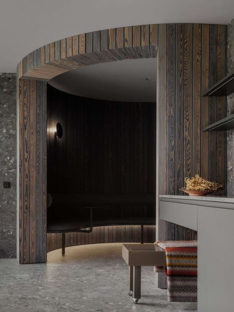 Curved interior hallway clad in dark burnt timber slats with integrated seating alcove and soft ambient lighting.