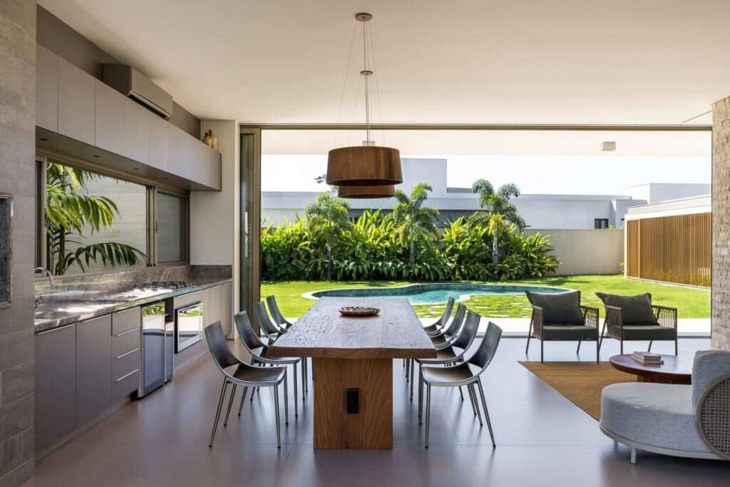 Open-plan dining kitchen interior with a solid wooden dining table, modern cabinetry, and pocket glass doors opening to the outdoor pool and lawn.