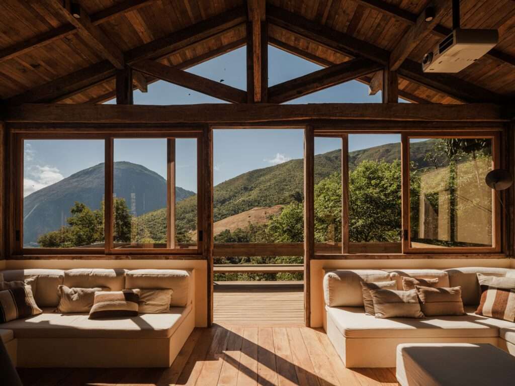 View from inside Japú House living room looking out through large wood-framed sliding glass doors to mountain peak views.