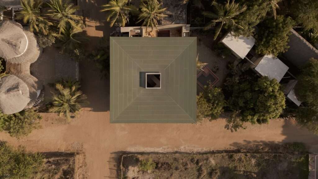 Directly overhead top-down drone shot of Suuel Living square roof structure with central skylight surrounded by dirt roads and palm trees.