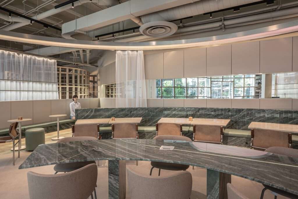 Curved green quartzite communal table with integrated power outlets and surrounding seating at Raheeq Ohm.