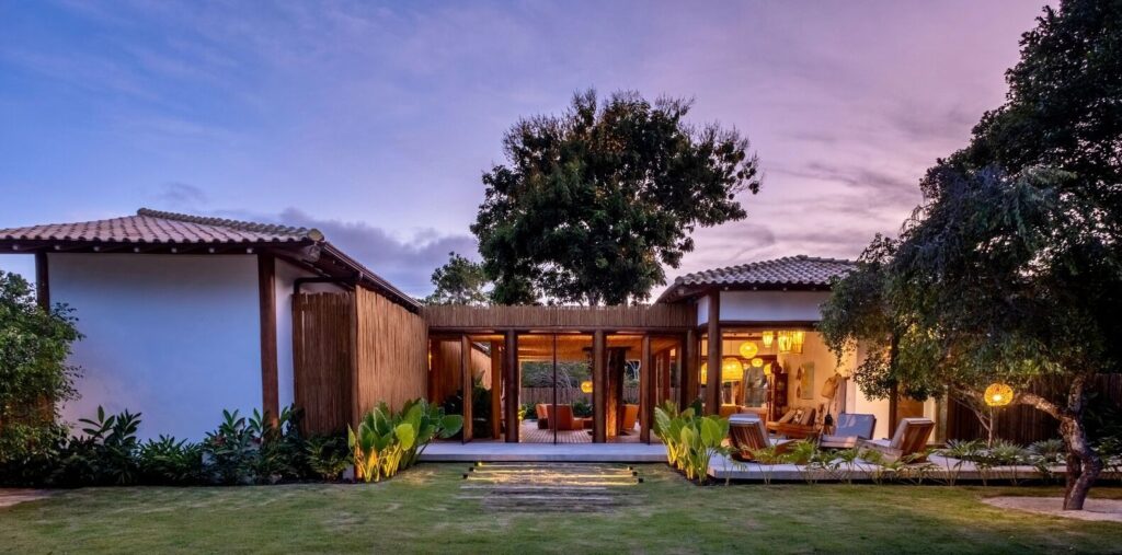 Exterior evening view of Ichiguin House illuminated with warm interior lighting and outdoor spotlights amidst tropical landscaping.