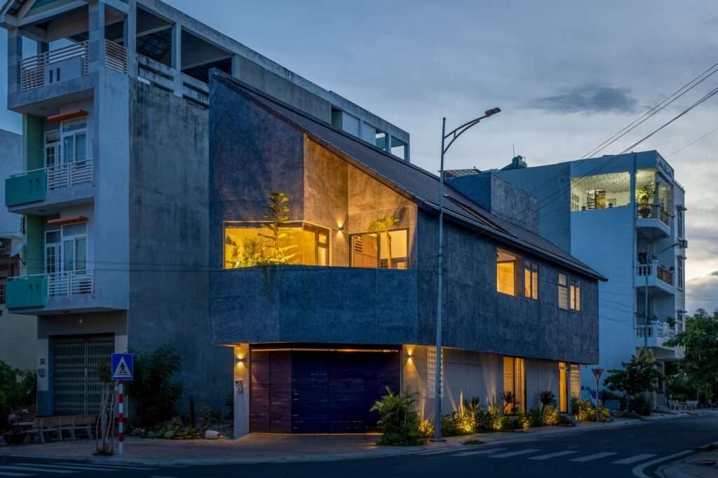 Evening twilight view of the Inner Courtyard House with warm interior lighting glowing through strategically placed window openings and upper balcony cutouts.