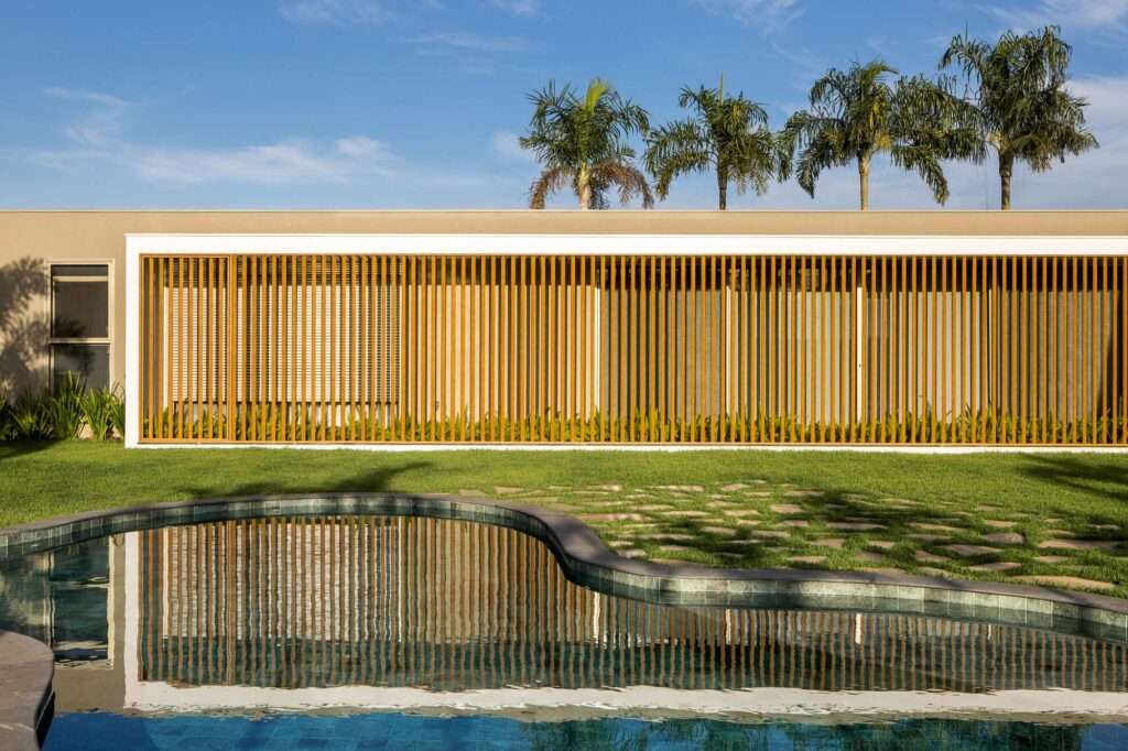 Close-up elevation of vertical wooden brise-soleil solar louvers on the private wing reflecting in the organic swimming pool water.
