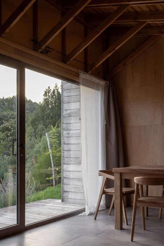 Large glass sliding door beside a wooden dining table opening onto a timber deck and green lawn.