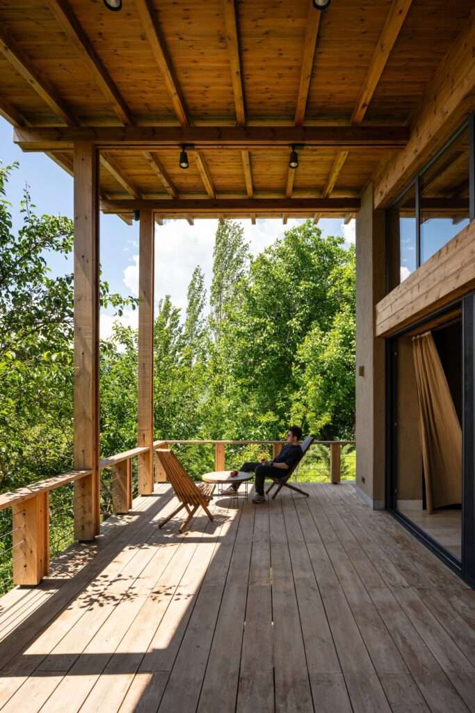 Covered upper wooden terrace overlooking dense green trees with outdoor lounge chairs.