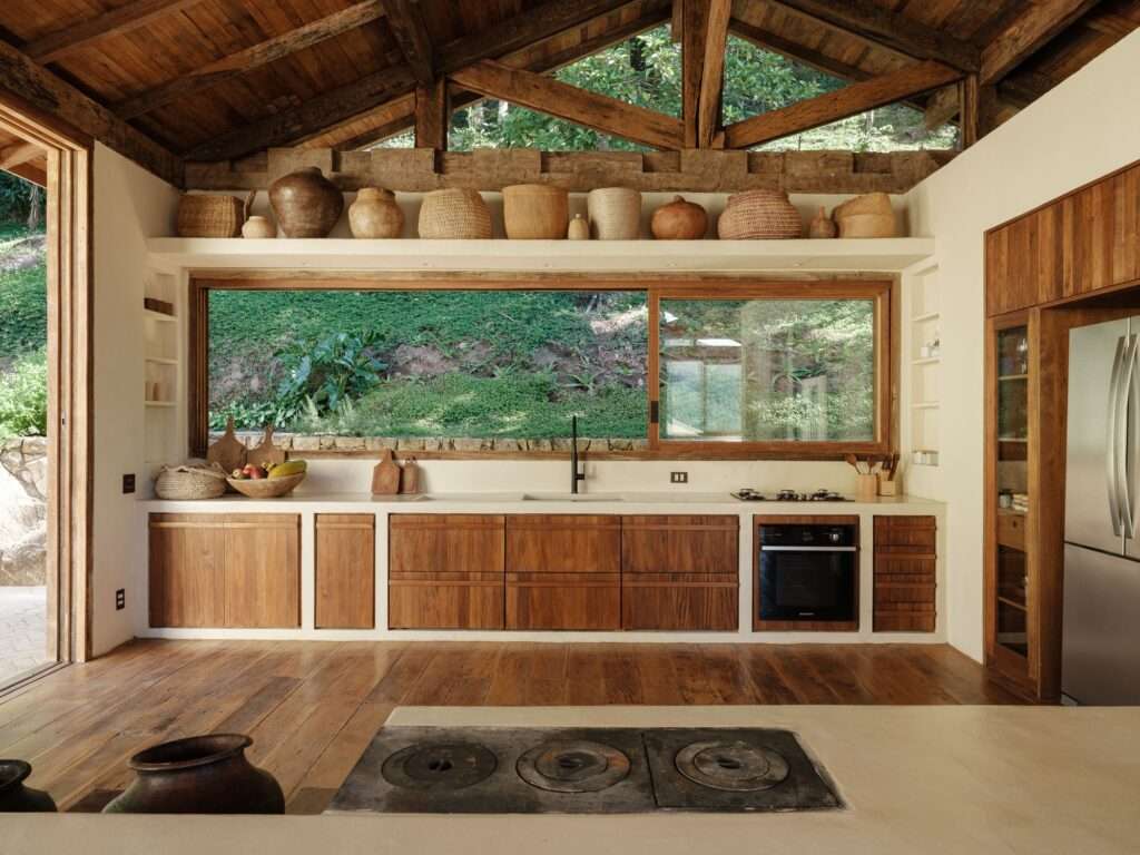Open kitchen in Japú House with wooden cabinets, white plaster counters, and a horizontal ribbon window facing the rear embankment.