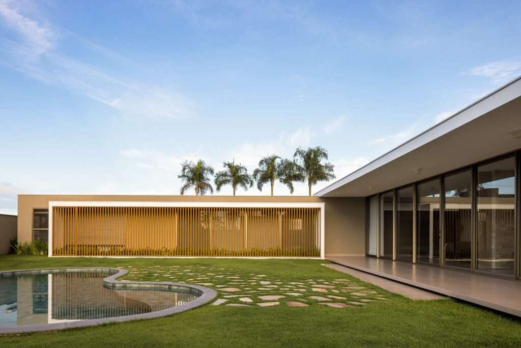Wide view of Refugio House showing the intersection between the louvered private wing, central lawn, organic pool, and cantilevered social terrace.
