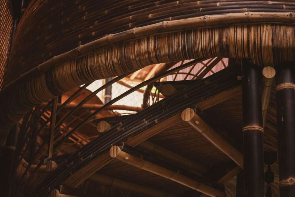 Close-up detailed interior shot of complex bamboo joinery, showing the connection between a large dark bamboo column, woven bamboo panels, and a series of smaller bamboo poles forming a layered edge.