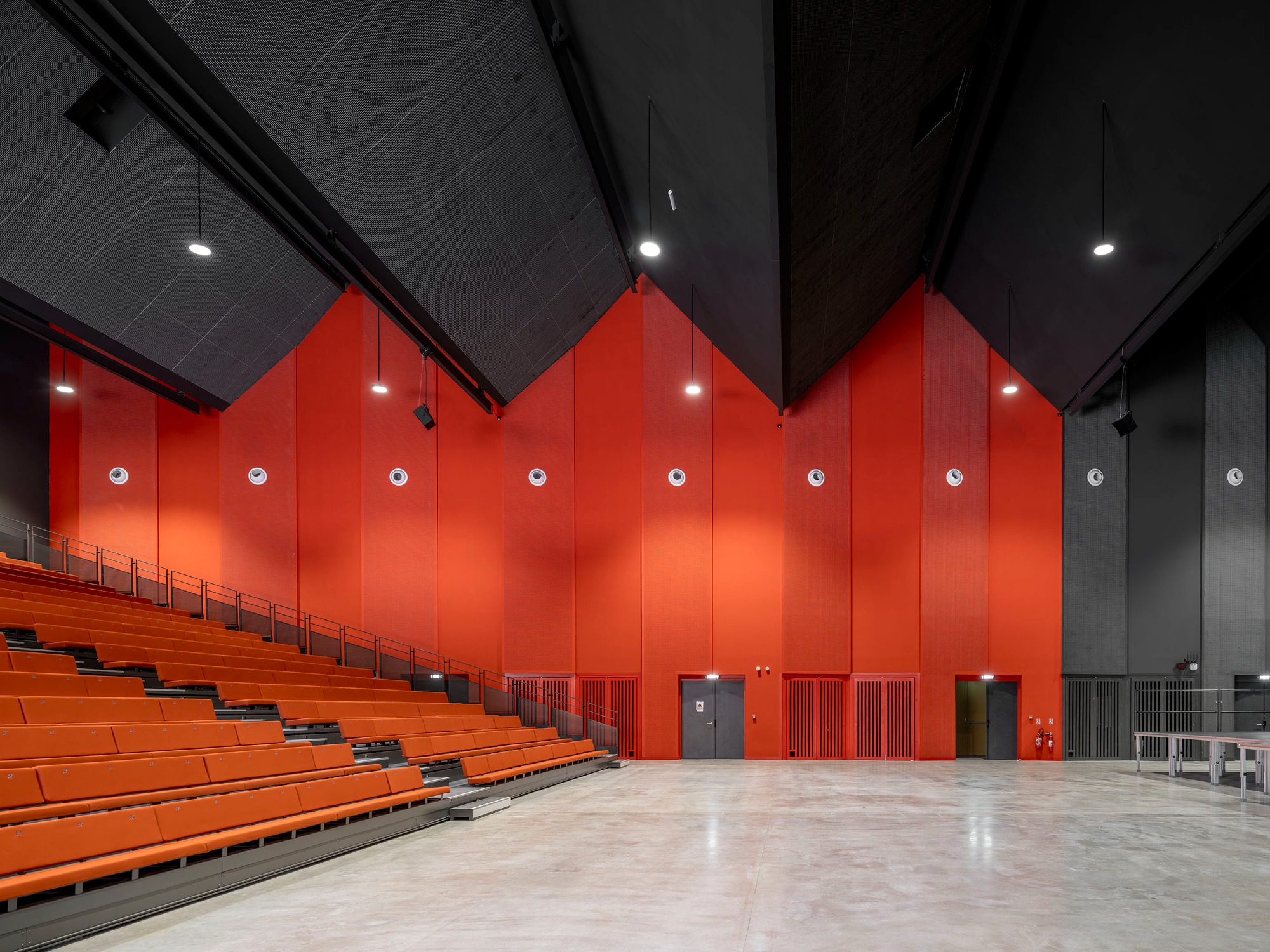 Orange tiered seats beside red wall panels and circular openings under a dark pitched ceiling at La Tuilerie.