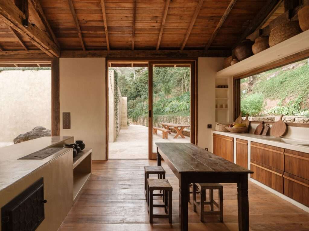 Dining area inside Japú House opening onto an intermediate stone courtyard between the house and the hillside.