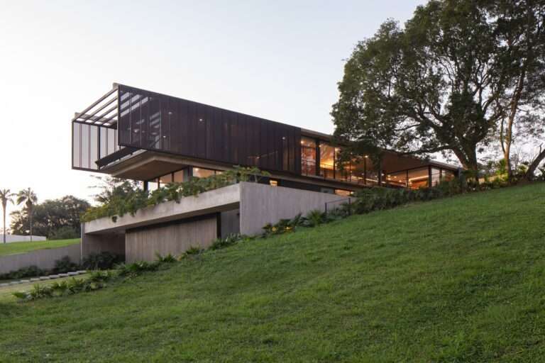 Wide exterior view of Casa Galería built into a grassy green slope, showing the tiered concrete foundation and cantilevered upper floor at dusk.