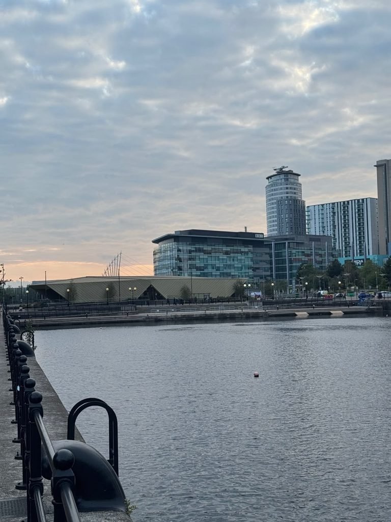 ممشى الواجهة المائية ينظر عبر المياه باتجاه مباني MediaCityUK في سالفورد كيز تحت سماء غائمة
