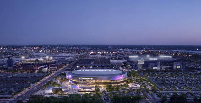 Aerial nighttime view of circular sports arena with LED screens and surrounding parking areas