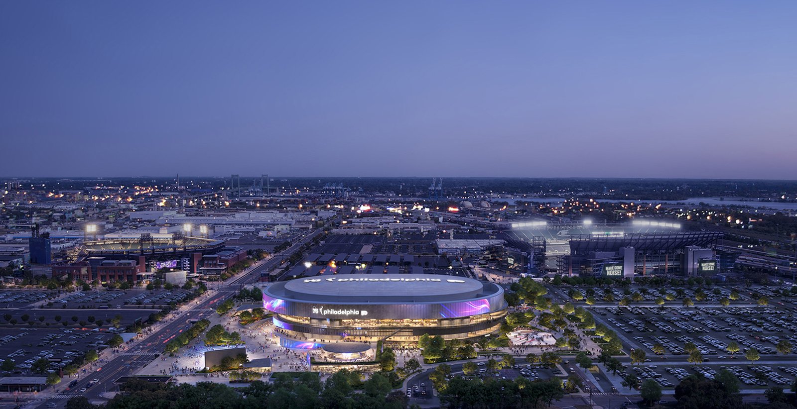 Aerial nighttime view of circular sports arena with LED screens and surrounding parking areas
