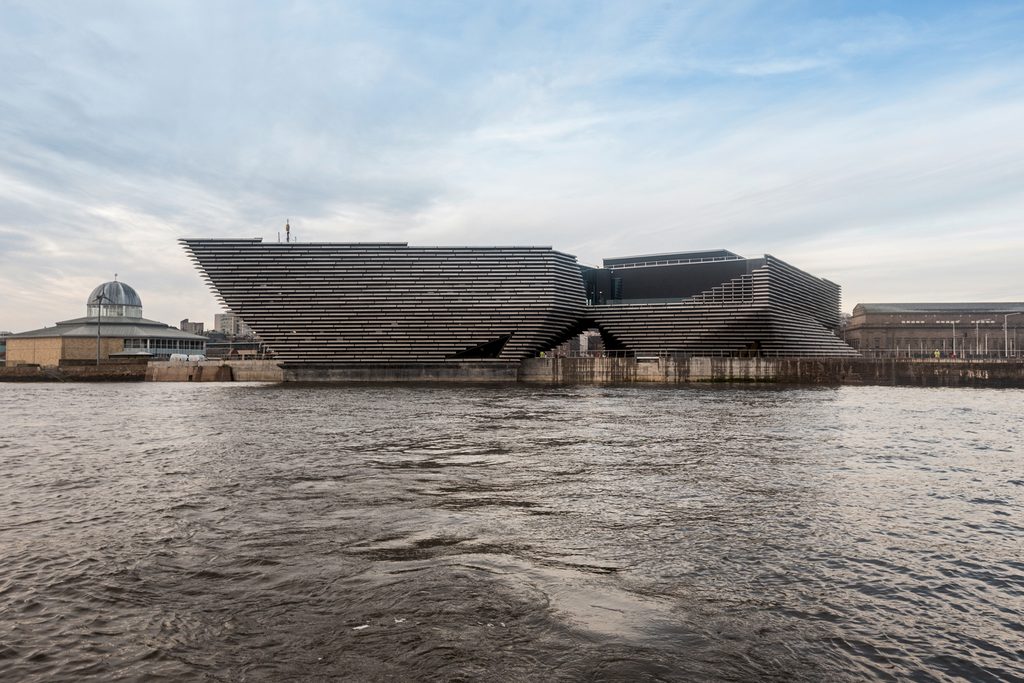 Exterior view of the V&A Dundee building featuring horizontal stone cladding modules over water.