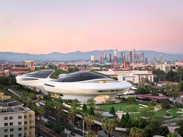 Aerial view of the curved Lucas Museum building surrounded by green parkland and the Los Angeles skyline.