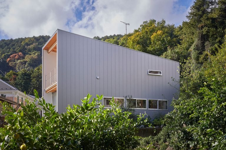 Two-story exterior facade framed by surrounding trees and lush foliage under a blue sky.