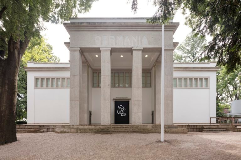 Symmetrical stone portico and entrance facade of the German Pavilion set amidst trees.