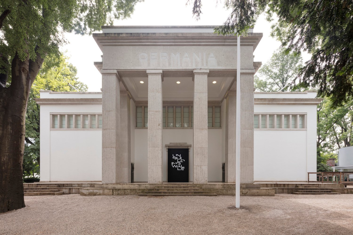 Symmetrical stone portico and entrance facade of the German Pavilion set amidst trees.