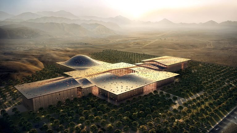 Aerial view showing complex building massing, central canopy structure, and surrounding landscaped grounds.