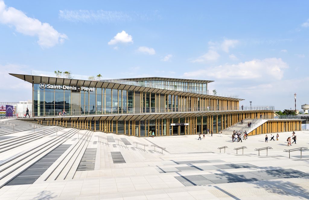 Multi-tiered glass facade with vertical timber louvers fronted by a large public plaza.