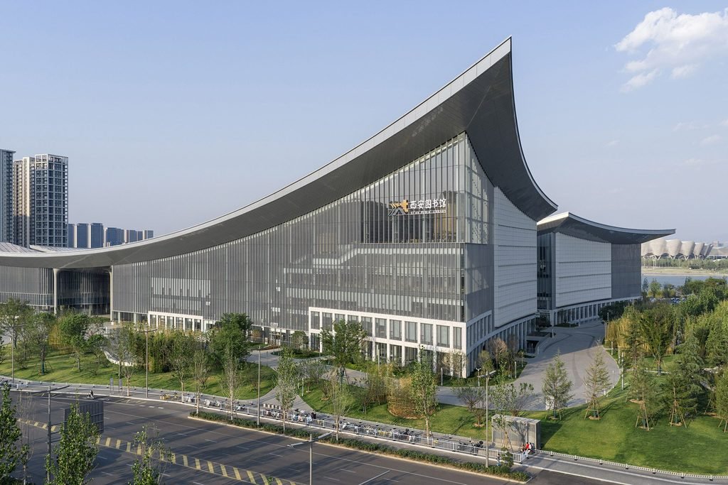 Modern library building exterior showing upward-curved roof corner and extensive glazed enclosure.