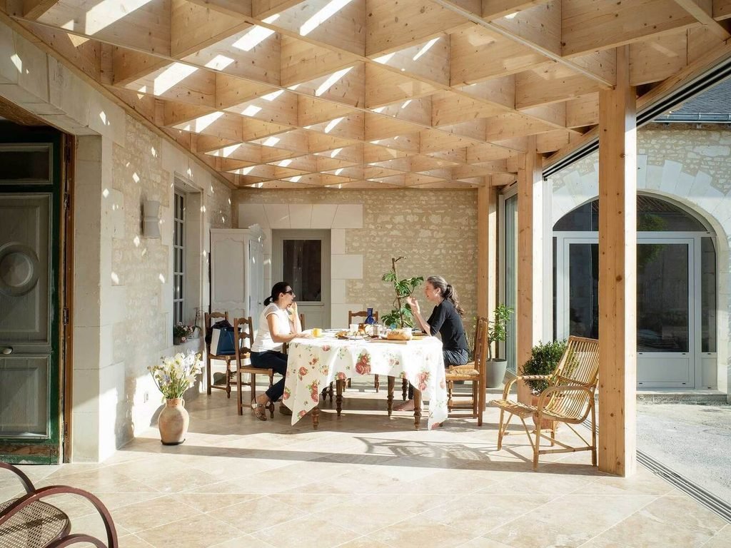 Two people seated at a table under a coffered timber canopy in a stone courtyard.