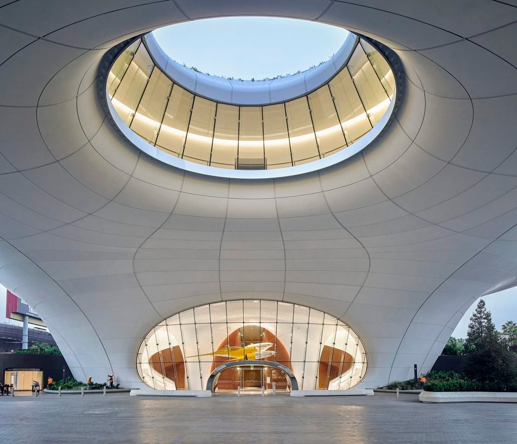 Looking up at a central elliptical oculus opening within a sheltered underside canopy plaza.