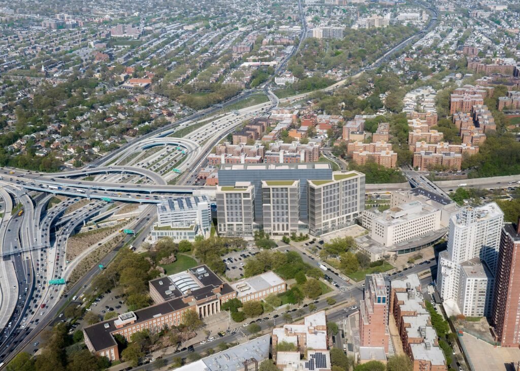 High aerial view of the Kew Gardens site showing three housing towers adjacent to highway infrastructure.
