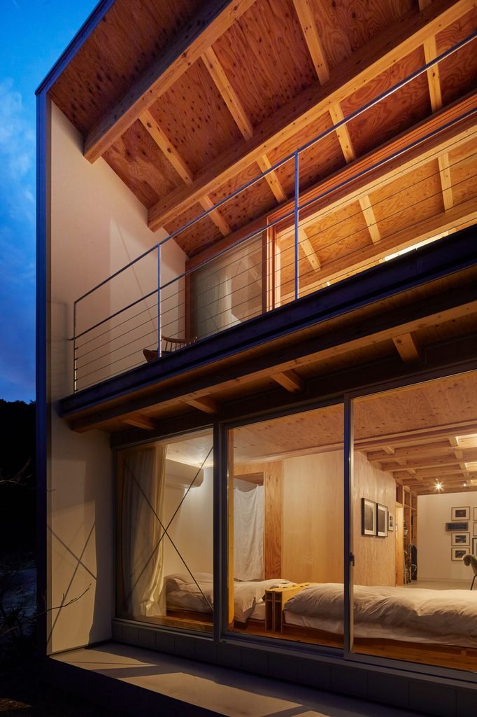 Two-story exterior at dusk showing warmly illuminated glass sliding doors and upper timber ceiling.