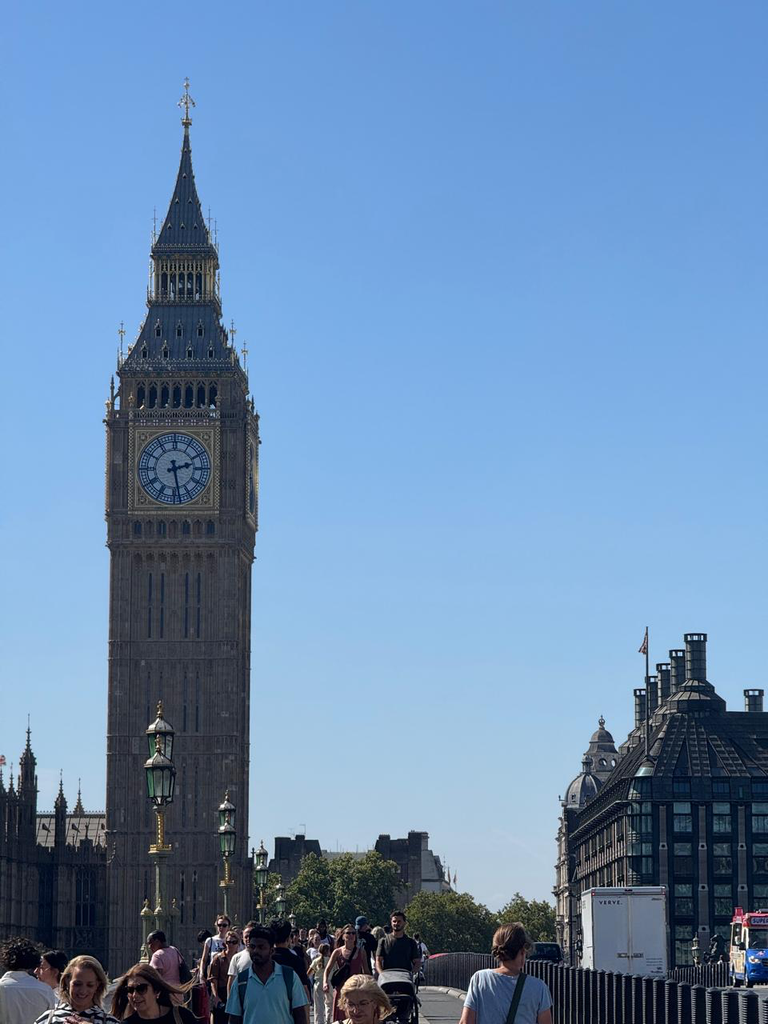 The Elizabeth Tower clock tower against a clear blue sky with pedestrians walking across Westminster Bridge